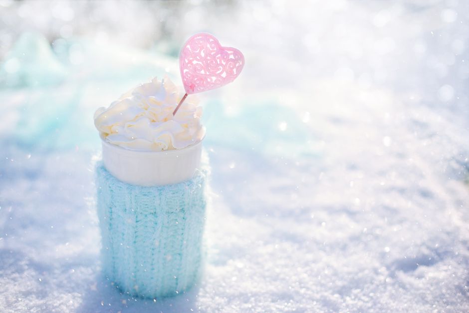 Warm beverage topped with cream in snow, perfect for winter themes.